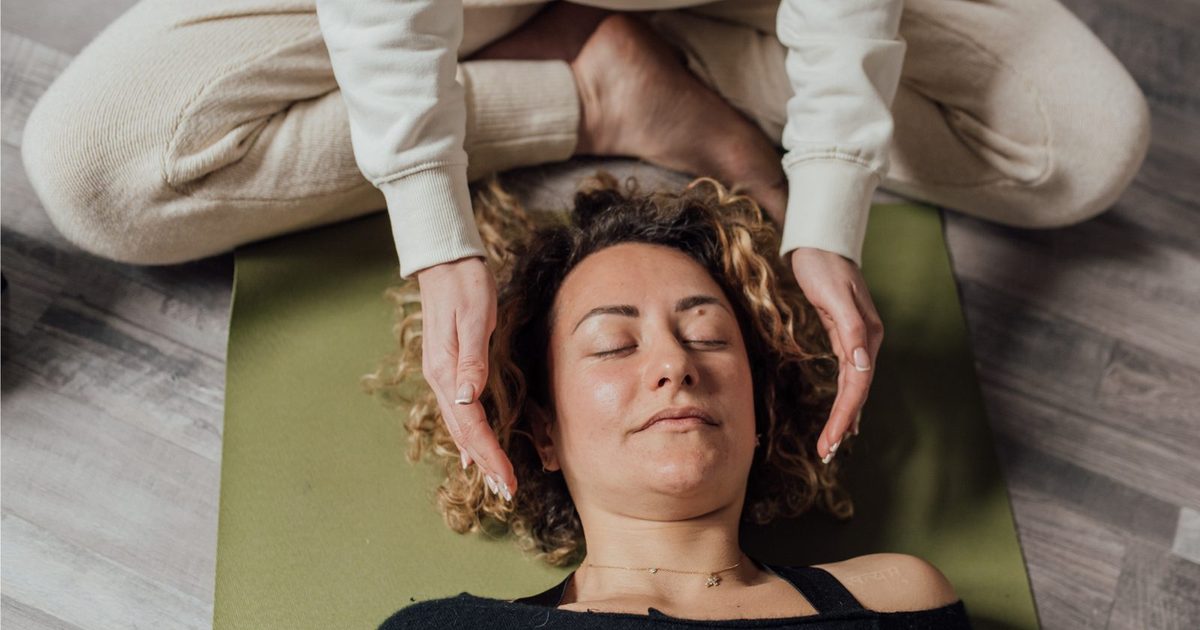 A practitioner holding her hands gently near a relaxed client's head during an energy healing session