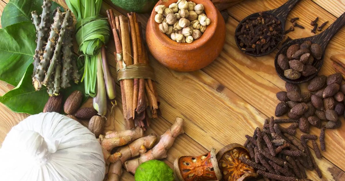 Ayurvedic herbs and spices, including cinnamon, cloves and fresh turmeric, on a wooden table