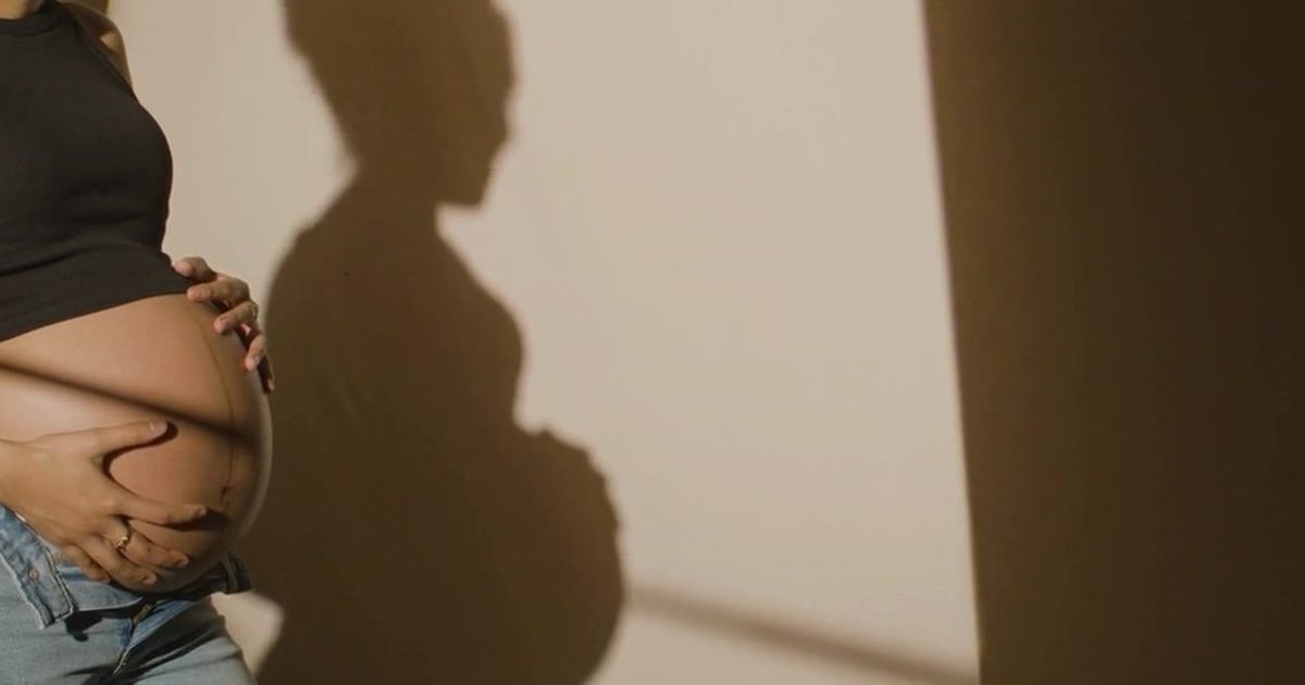 A pregnant woman cradling her belly in soft afternoon light