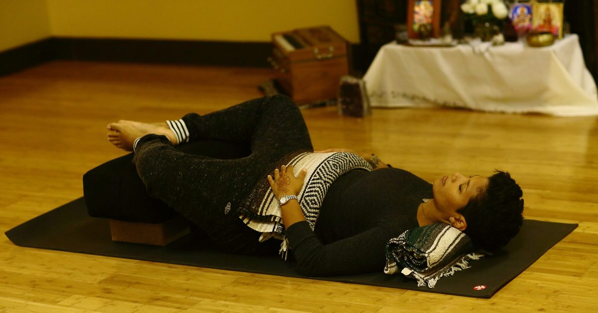 A student resting on a bolster under a blanket in a restorative yoga pose