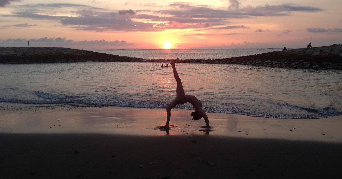 A yogi in a backbend on the beach at sunset with the ocean behind