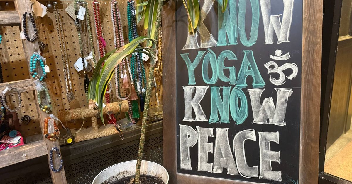 Yoga gear and malas hanging beside a chalkboard that reads Know Yoga Know Peace in the studio shop