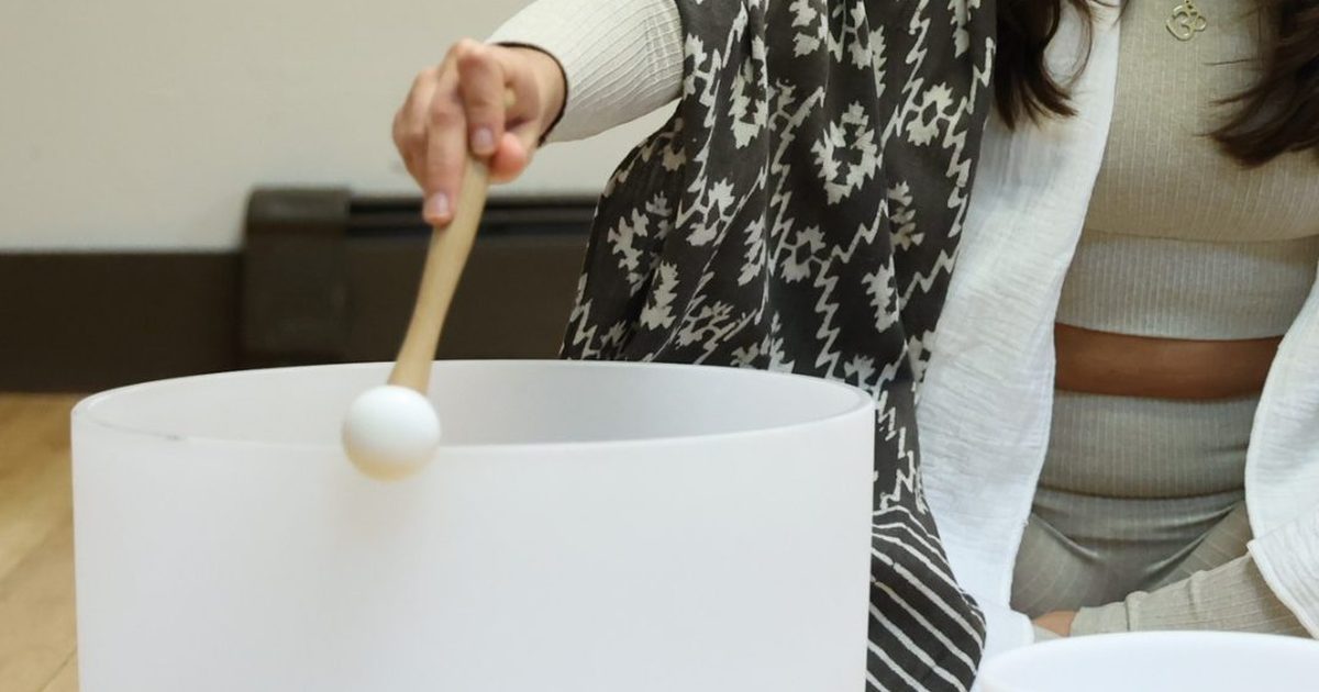 A practitioner playing a large white crystal singing bowl with a mallet