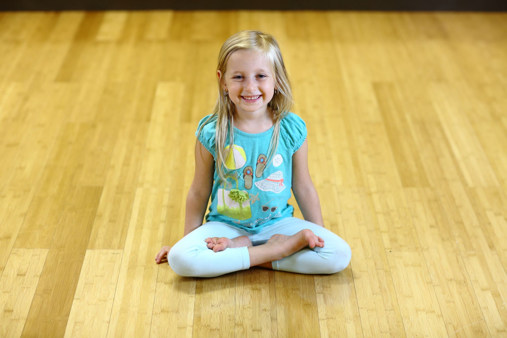 Smiling girl sitting cross-legged in a kids yoga class at Revolution Yoga