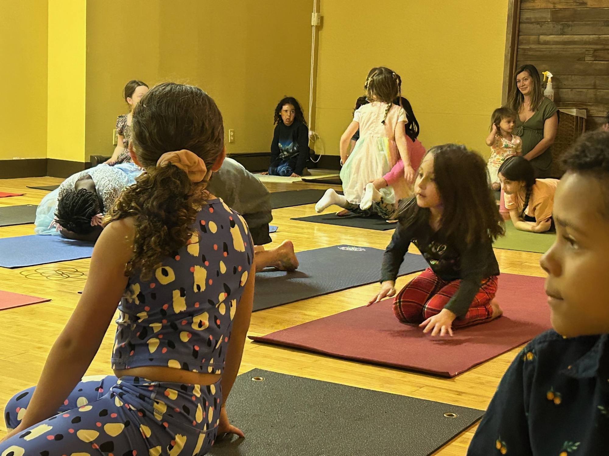 Children seated on yoga mats listening during a family yoga celebration