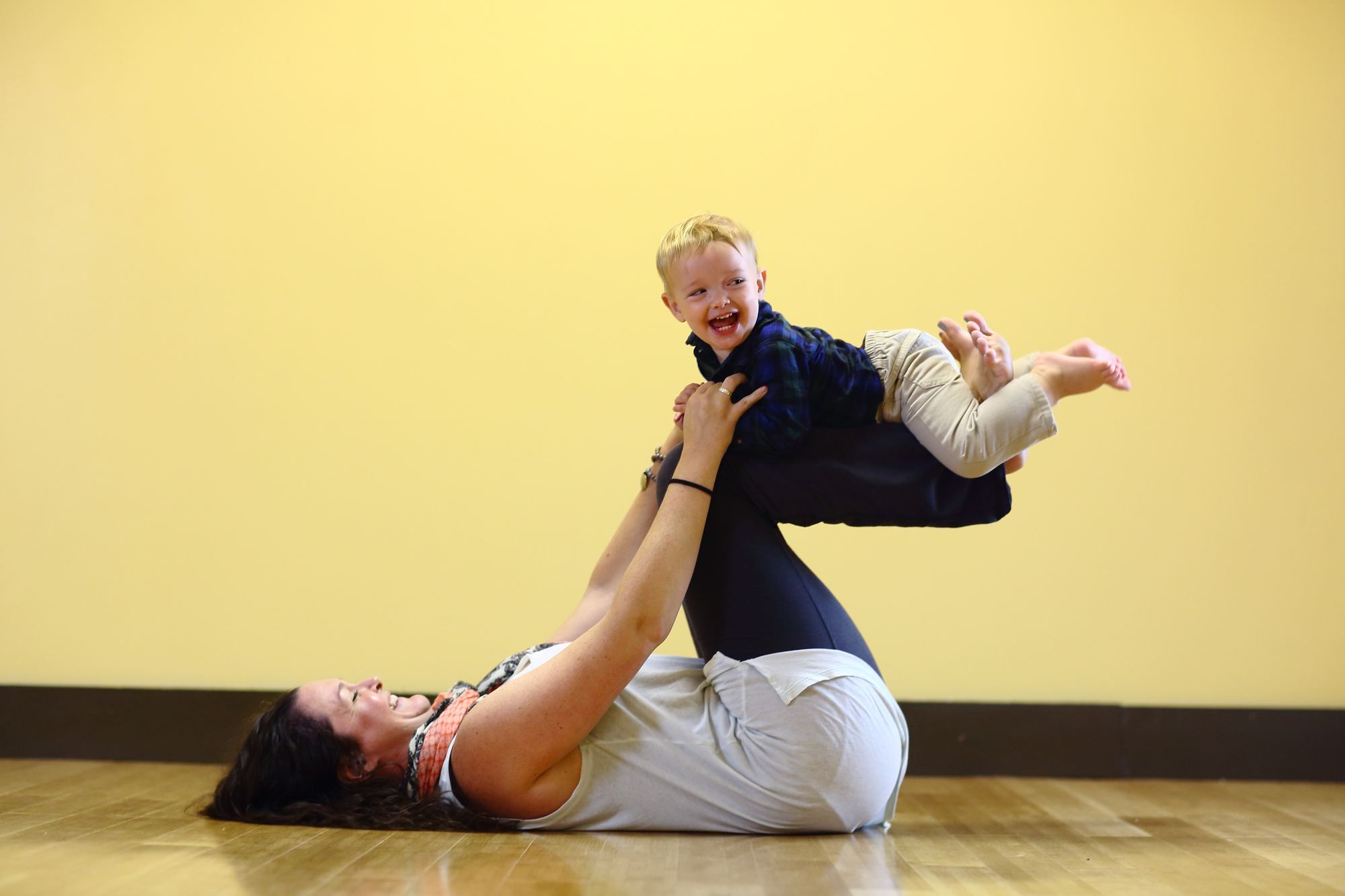 Toddler laughing in airplane pose with his mom during a Mommy and Me class