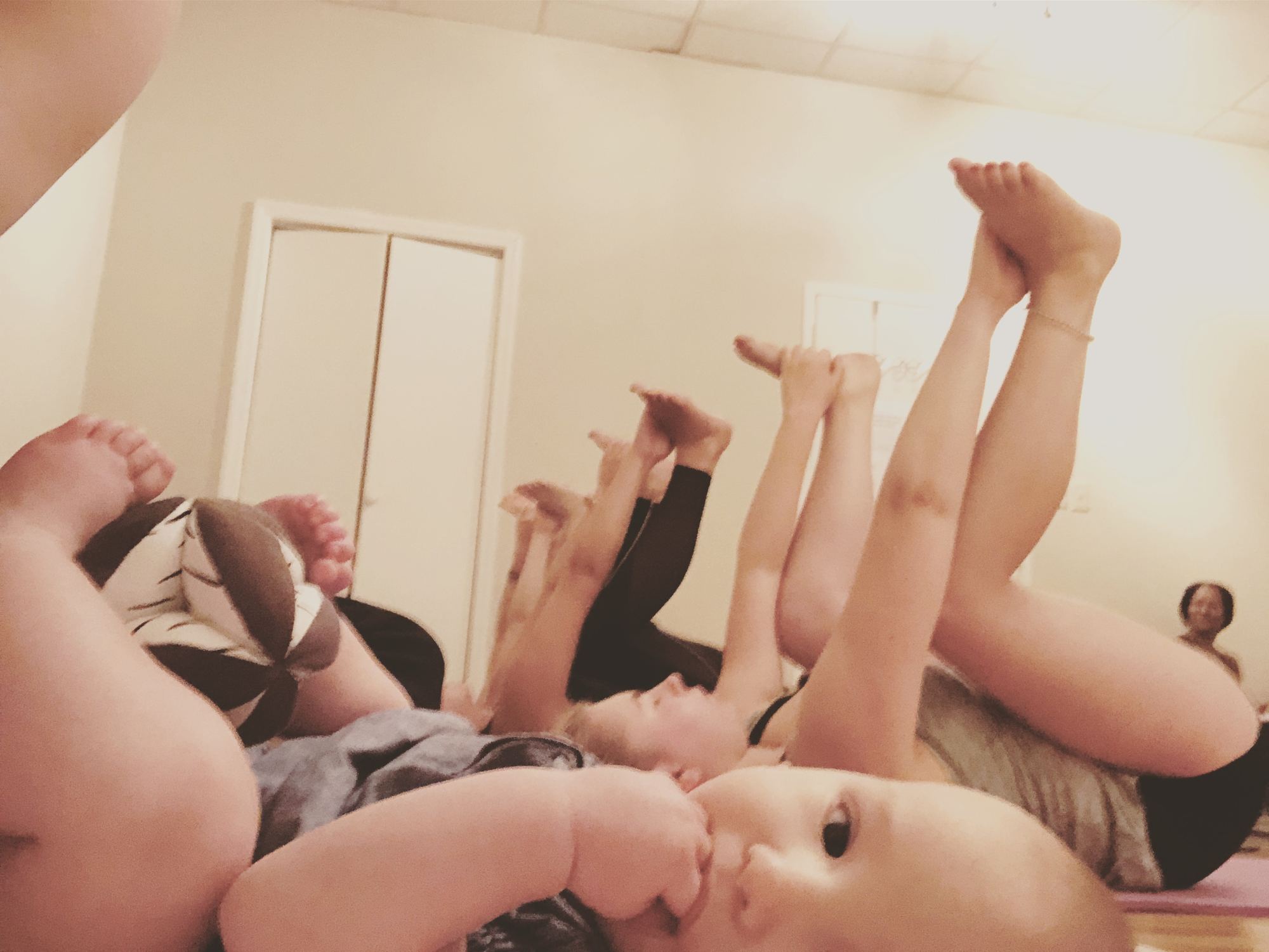 Moms and babies with legs raised during a Mommy and Me yoga class