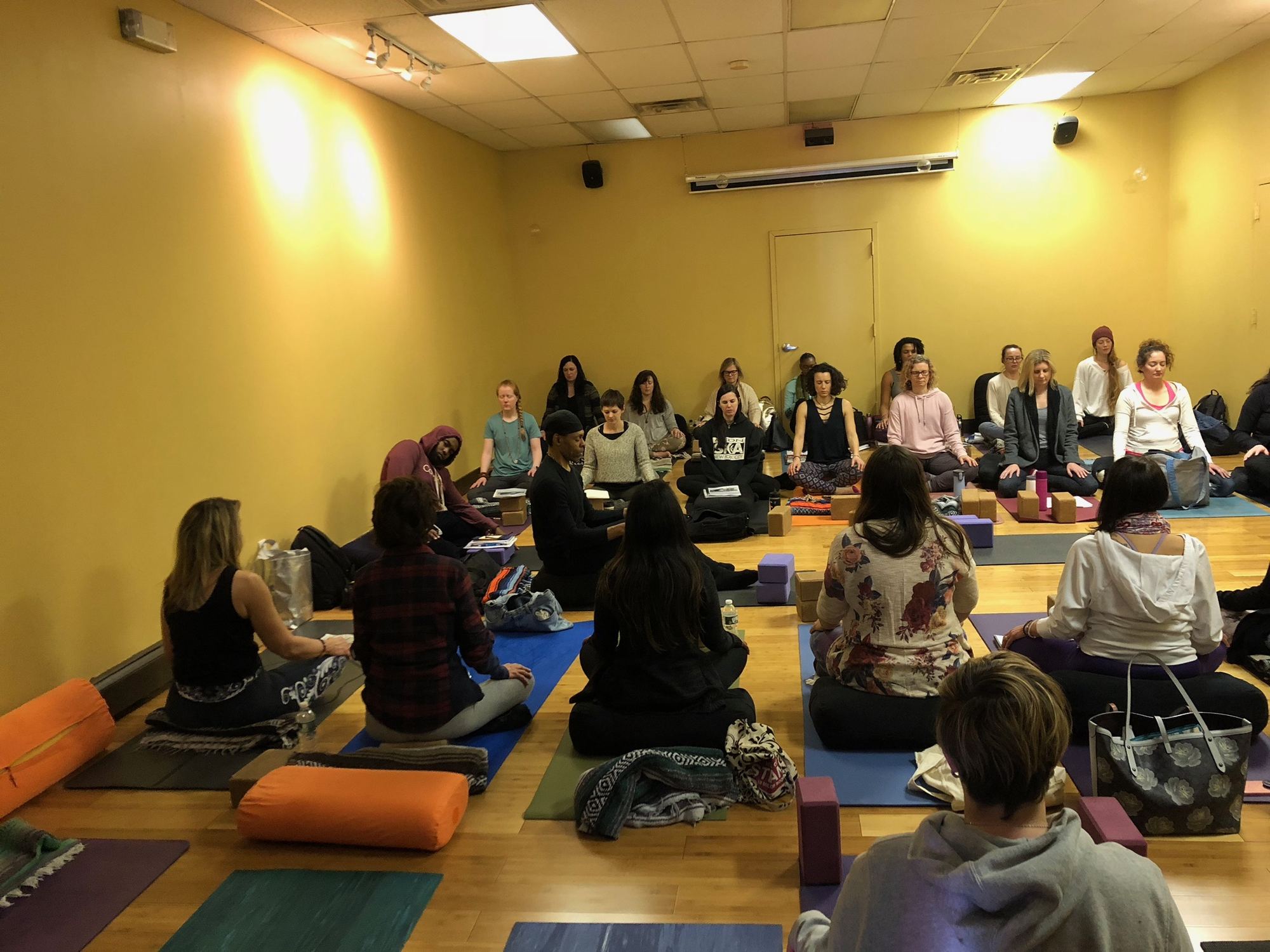 Large group seated on mats for a community gathering in the Revolution Yoga studio