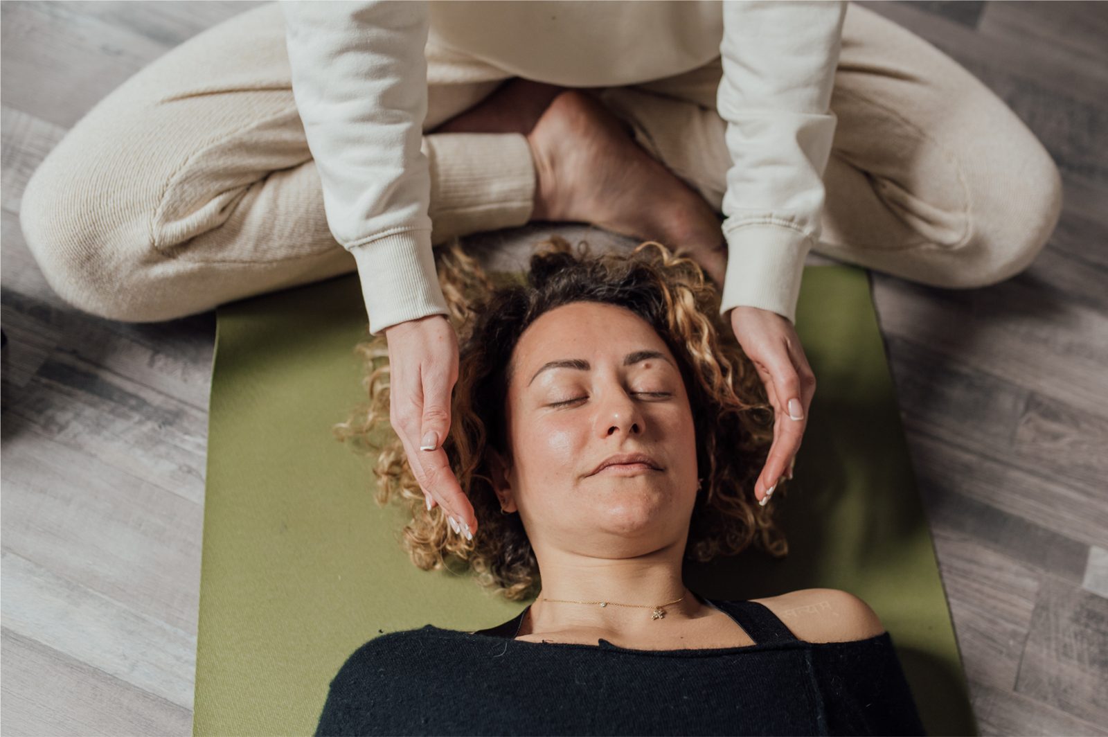 Reiki session: practitioner hands hovering around a resting client on a yoga mat