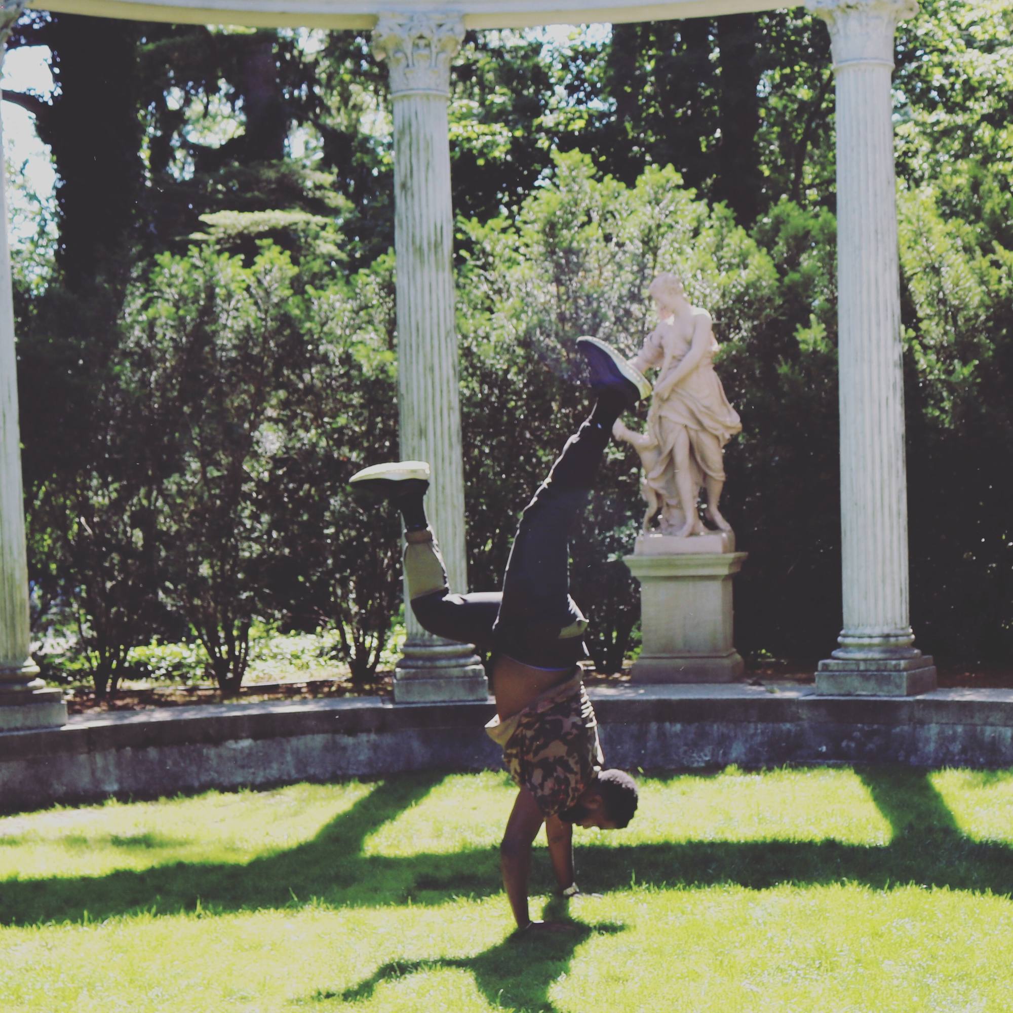 Handstand beside a classical statue and columns in a garden