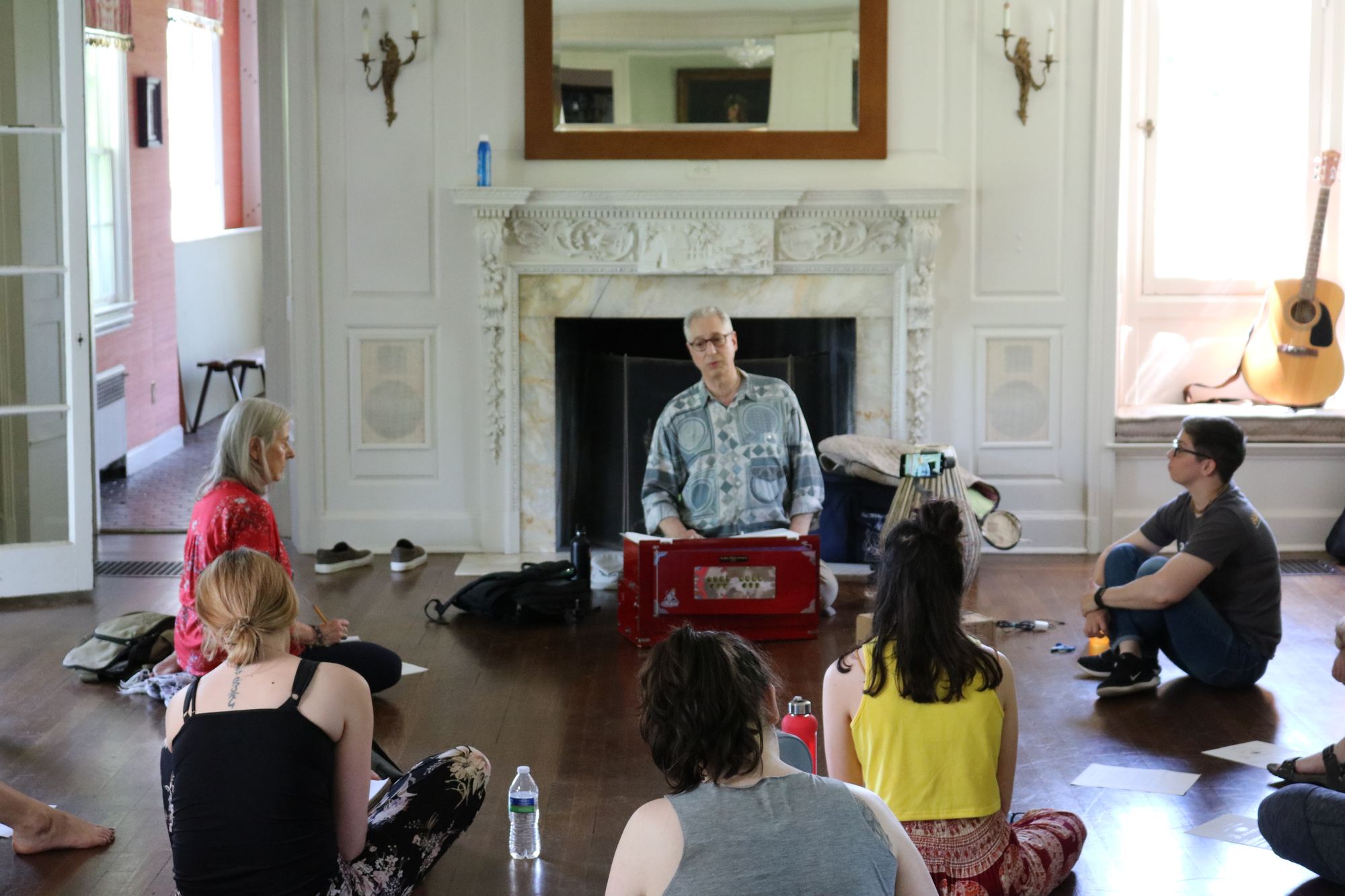 Teacher leading a seated training session with a harmonium, students gathered around