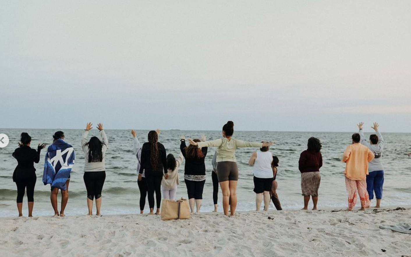 Women's Circle gathering on the beach, arms raised toward the ocean