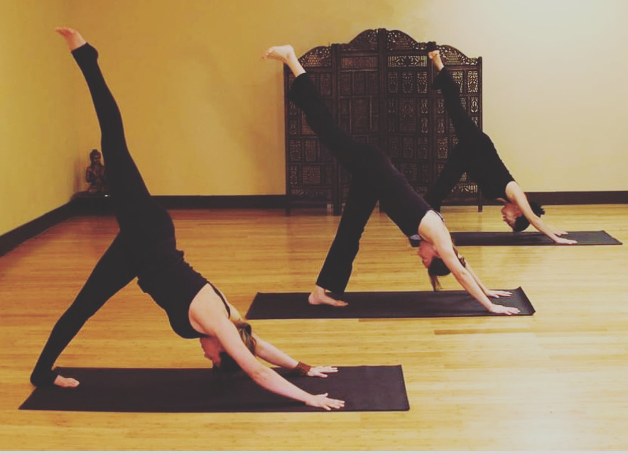 Students in three-legged downward dog in a small group class