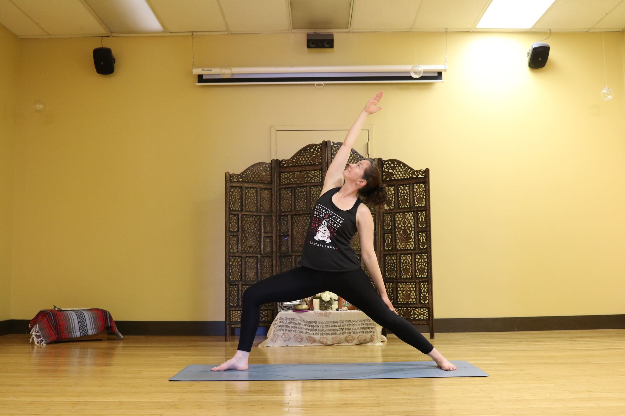 Yoga teacher in reverse warrior in front of the carved studio screen