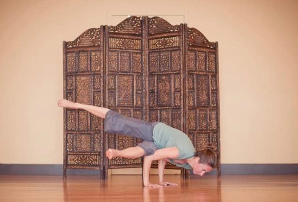 Yogi in crow pose in front of the carved wooden screen at Revolution Yoga