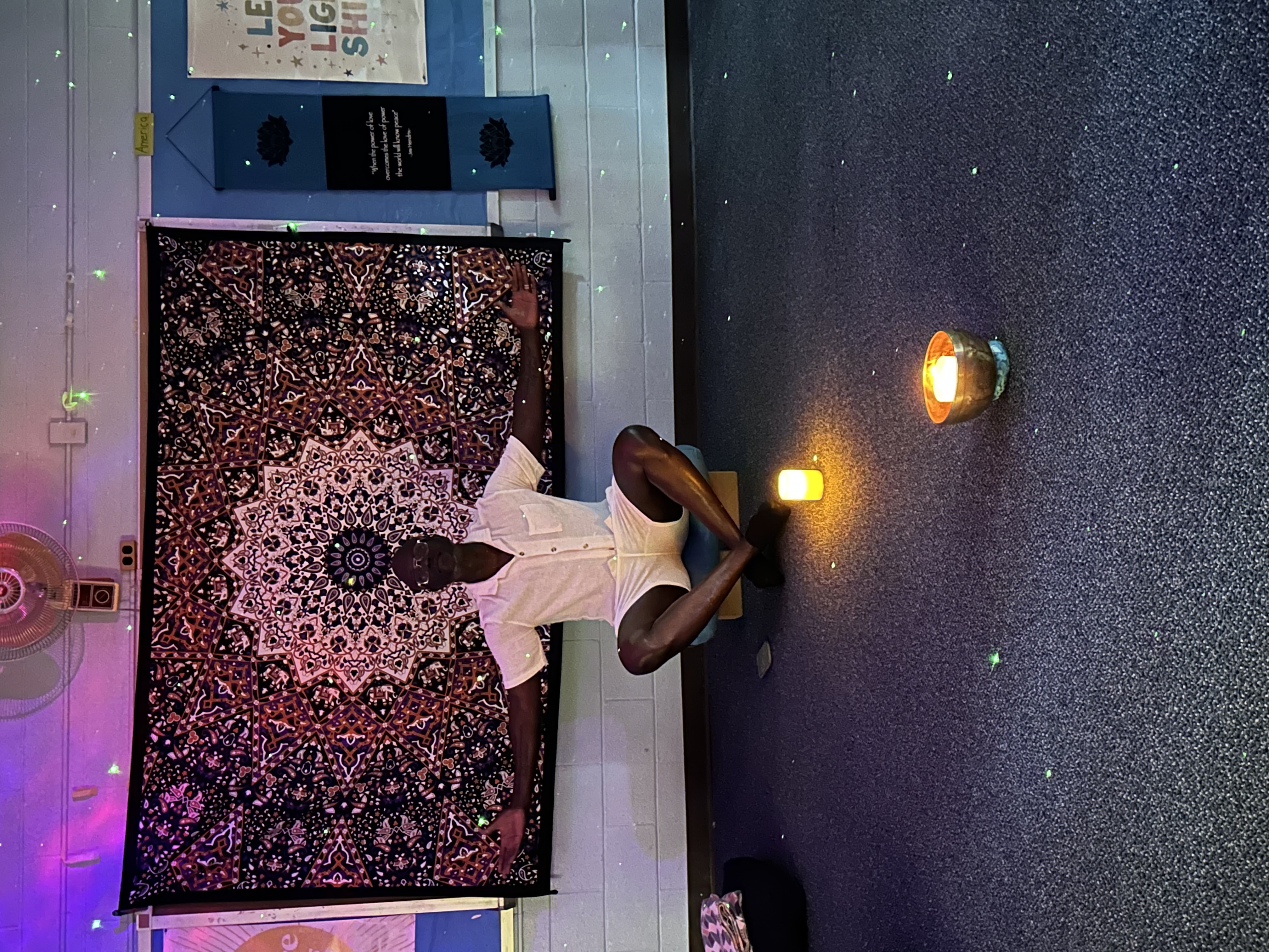 Anthony Heyward meditating by candlelight in front of a mandala tapestry